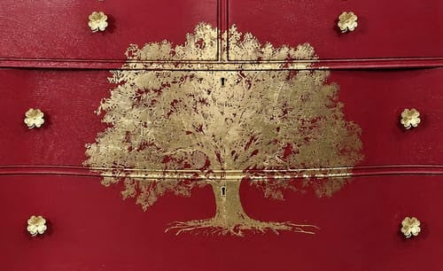 A red chest of drawers with a golden tree and gold clover knobs.
