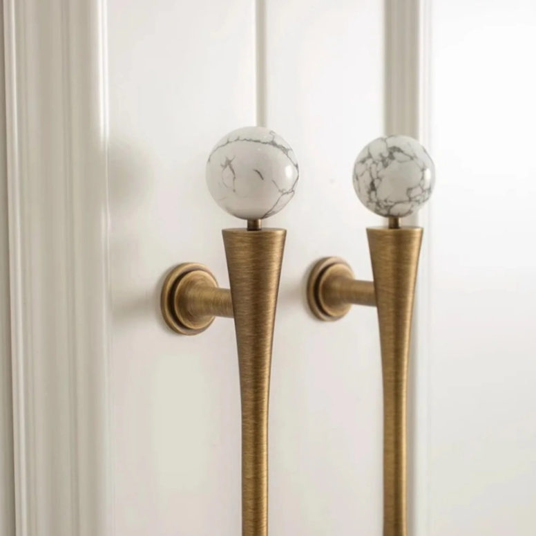 antique brass cabinet pulls on a white cabinet. They have white and grey marble balls on top. 