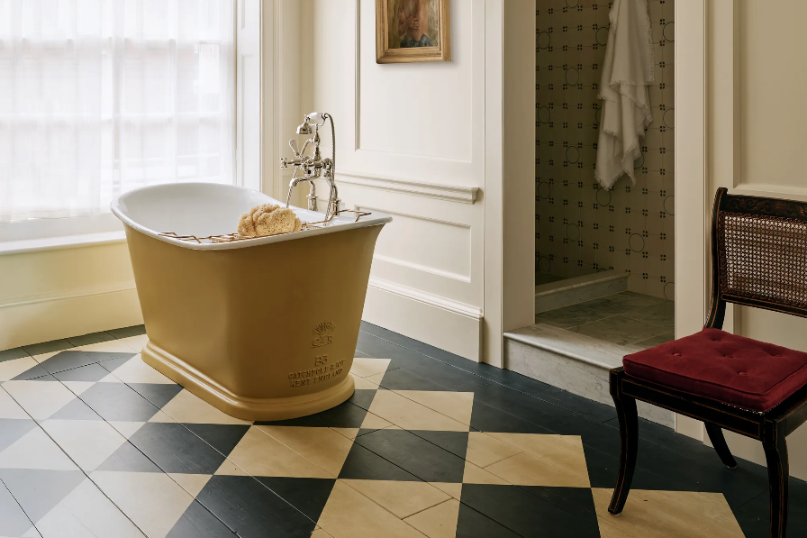 A yellow bath tub with a chequerboard floor. 