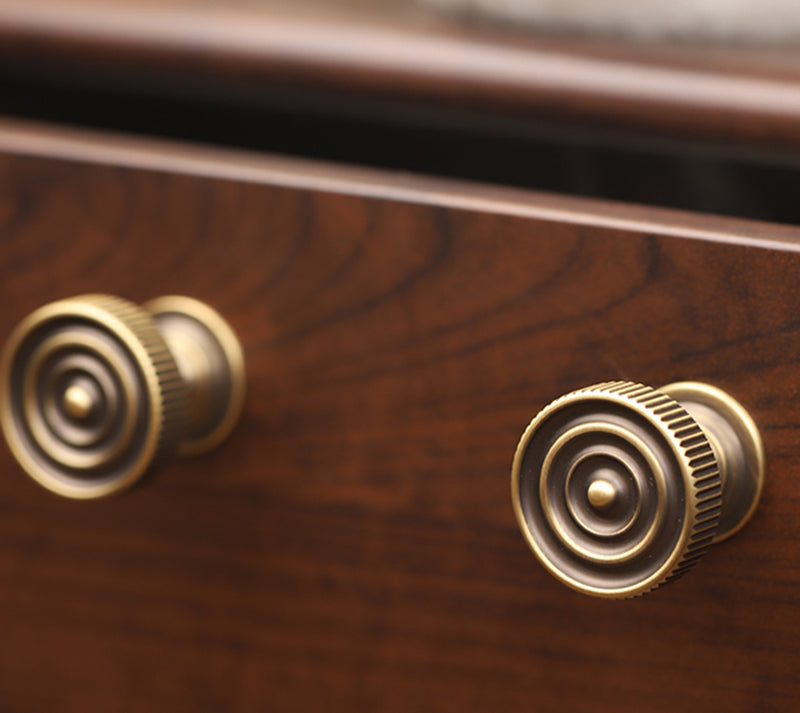 Two antique brass drawer handles on a mahogany drawer front. 